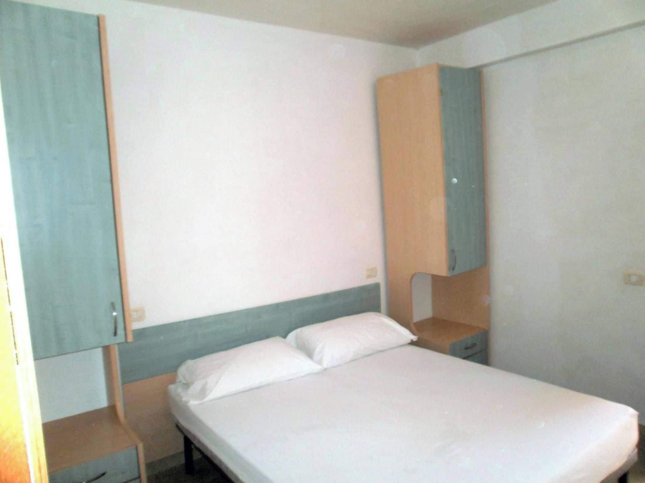 Una cama individual con ropa de cama blanca, una mesita de noche de madera y un armario con un panel azul claro.