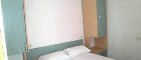 A single bed with white bedding, a wooden nightstand, and a wardrobe with a light blue panel.
