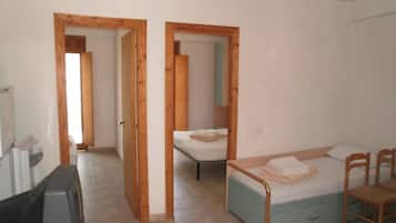Una stanza con un letto, una scrivania e una sedia. Porte in legno conducono a un'altra stanza.