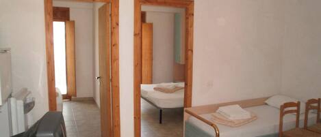 A room with a bed, a desk, and a chair. There are wooden doors leading to another room.