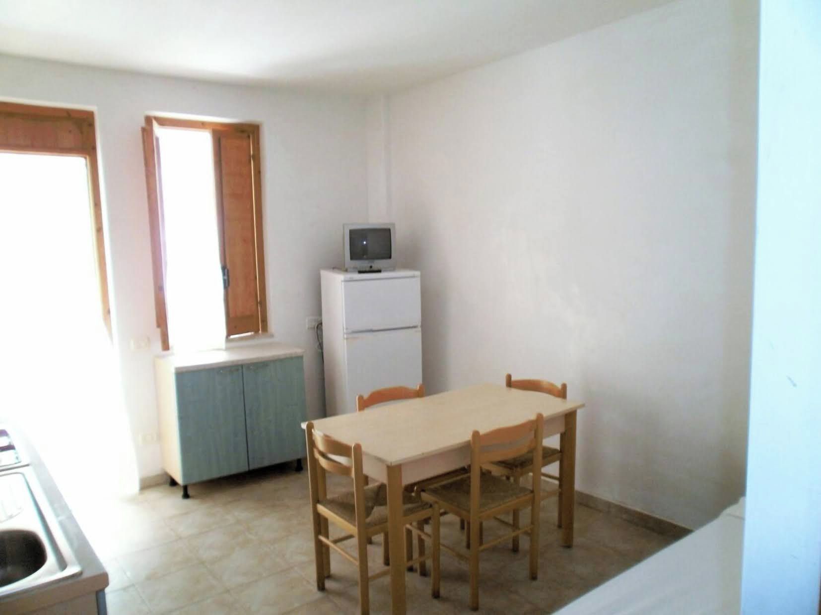 Una stanza piccola e modesta con un tavolo da pranzo, sedie, un televisore su un supporto e una finestra con tende.