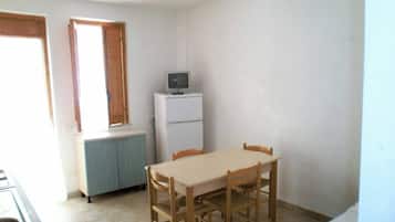 Una stanza piccola e modesta con un tavolo da pranzo, sedie, un televisore su un supporto e una finestra con tende.