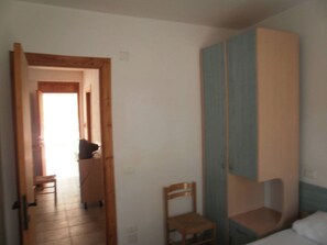 Una habitación con una cama, una silla de madera, un armario y una puerta que da a otra estancia.