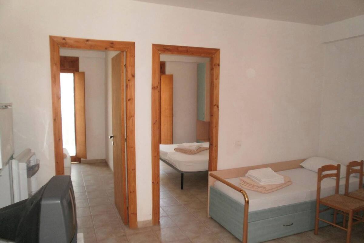 A room with a bed, a desk, and a chair. There are wooden doors leading to another room.