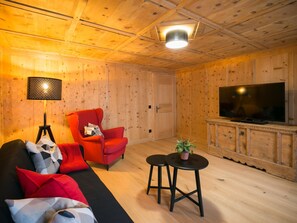 A wooden-paneled room with a sofa, two red chairs, a TV, and a lamp.