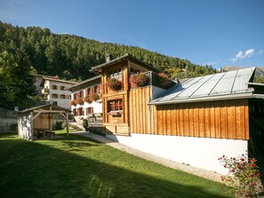 A chalet with a wooden facade, a balcony with flower boxes, and a mountain backdrop.