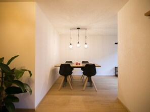 Un espace repas avec une table en bois, des chaises noires et des luminaires suspendus.