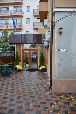 A hotel entrance with a reception desk, a paved courtyard, and a building with balconies. - La Casa Nord Hotel (Bucharest)