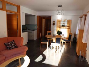 Un salon moderne avec un canapé, une table à manger et des chaises, une cuisine en arrière-plan et un lustre.