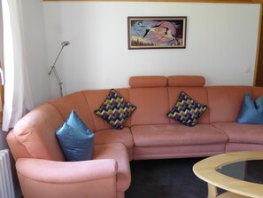 Un canapé rose agrémenté de coussins à motifs, une table basse avec un plateau en verre et une œuvre d’art encadrée accrochée au mur.
