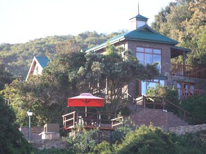 A two-story stone building with a green roof, a wooden deck, and a red umbrella.
