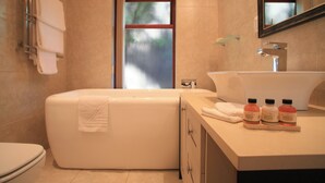 A modern bathroom with a bathtub, toilet, and vanity with a sink and three bottles of shampoo. - Under the Boardwalk Guest House (Wilderness)