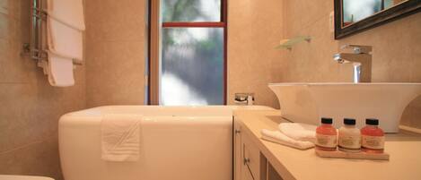A modern bathroom with a bathtub, toilet, and vanity with a sink and three bottles of shampoo.