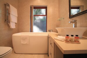 A modern bathroom with a bathtub, toilet, and vanity with a sink and three bottles of shampoo. - Under the Boardwalk Guest House (Wilderness)