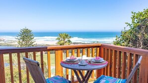 A wooden deck with two chairs and a small round table, overlooking a beach with ocean and greenery. - Under the Boardwalk Guest House (Wilderness)