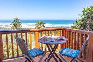 A wooden deck with two chairs and a small round table, overlooking a beach with ocean and greenery. - Under the Boardwalk Guest House (Wilderness)