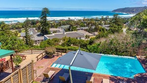 A pool with a view of the ocean, surrounded by houses and greenery. - Under the Boardwalk Guest House (Wilderness)