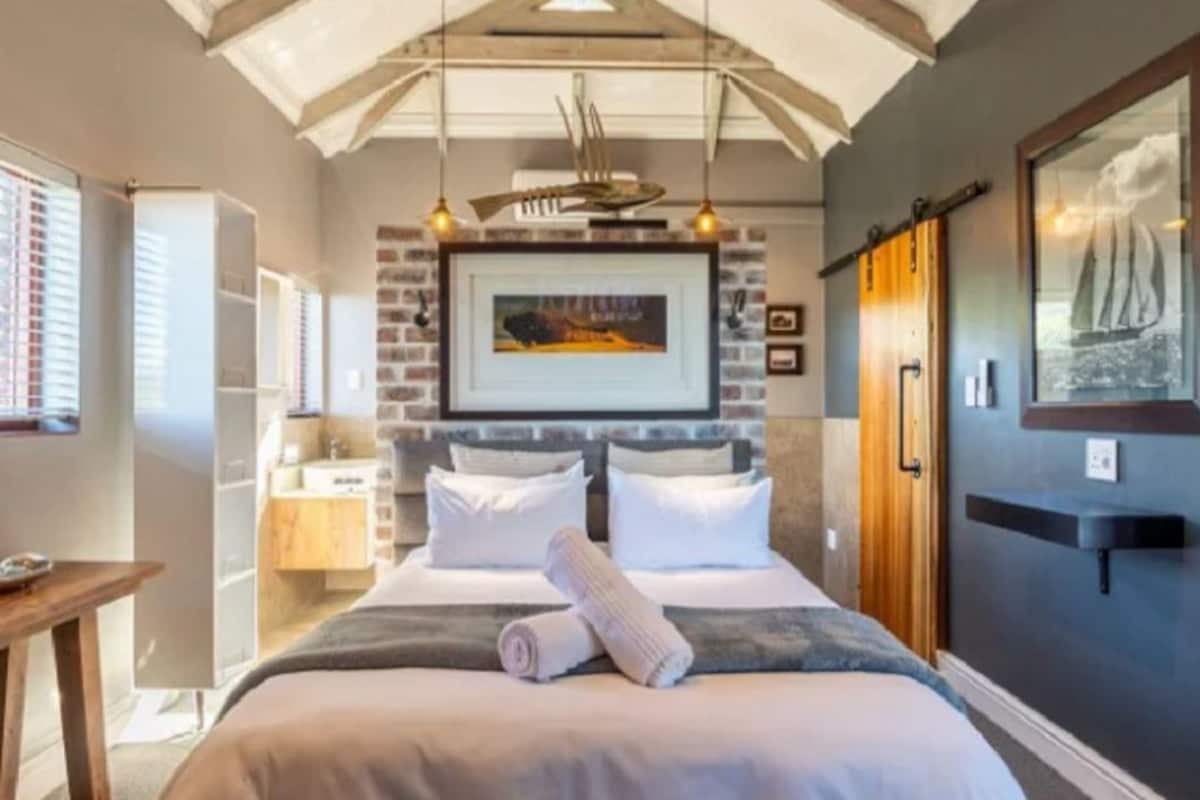 A bedroom with a bed, bedside tables, a hanging light fixture, a framed picture on the wall, and a window with blinds.