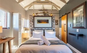 A bedroom with a bed, bedside tables, a hanging light fixture, a framed picture on the wall, and a window with blinds. - Under the Boardwalk Guest House (Wilderness)