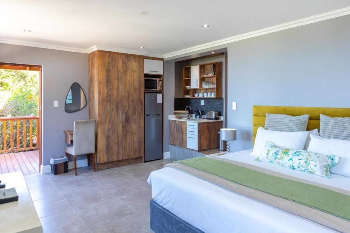A bedroom with a bed, a desk, a chair, a wardrobe, and a kitchenette.