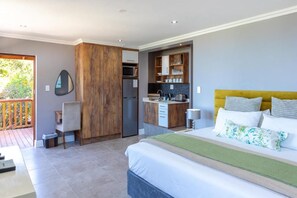 A bedroom with a bed, a desk, a chair, a wardrobe, and a kitchenette.