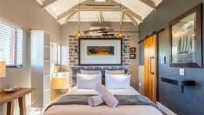 A bedroom with a bed, bedside tables, a hanging light fixture, a framed picture on the wall, and a window with blinds. - Under the Boardwalk Guest House (Wilderness)