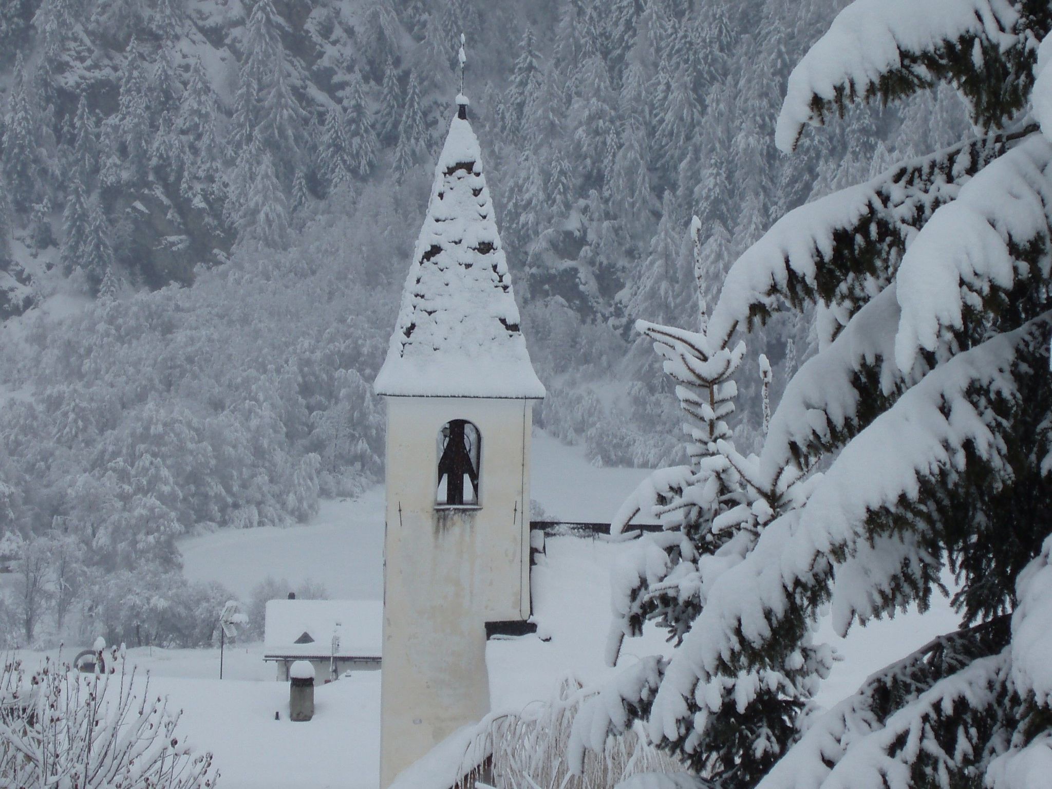 Eine schneebedeckte Kirche mit einem Glockenturm, umgeben von schneebedeckten Bäumen.