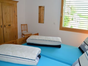 A bedroom with two beds, a wooden wardrobe, a chair, and a window with blinds. - Chasa Sumovia, (Sta. Maria - Santa Maria Val Müstair) by Interhome (Sta. Maria GR)