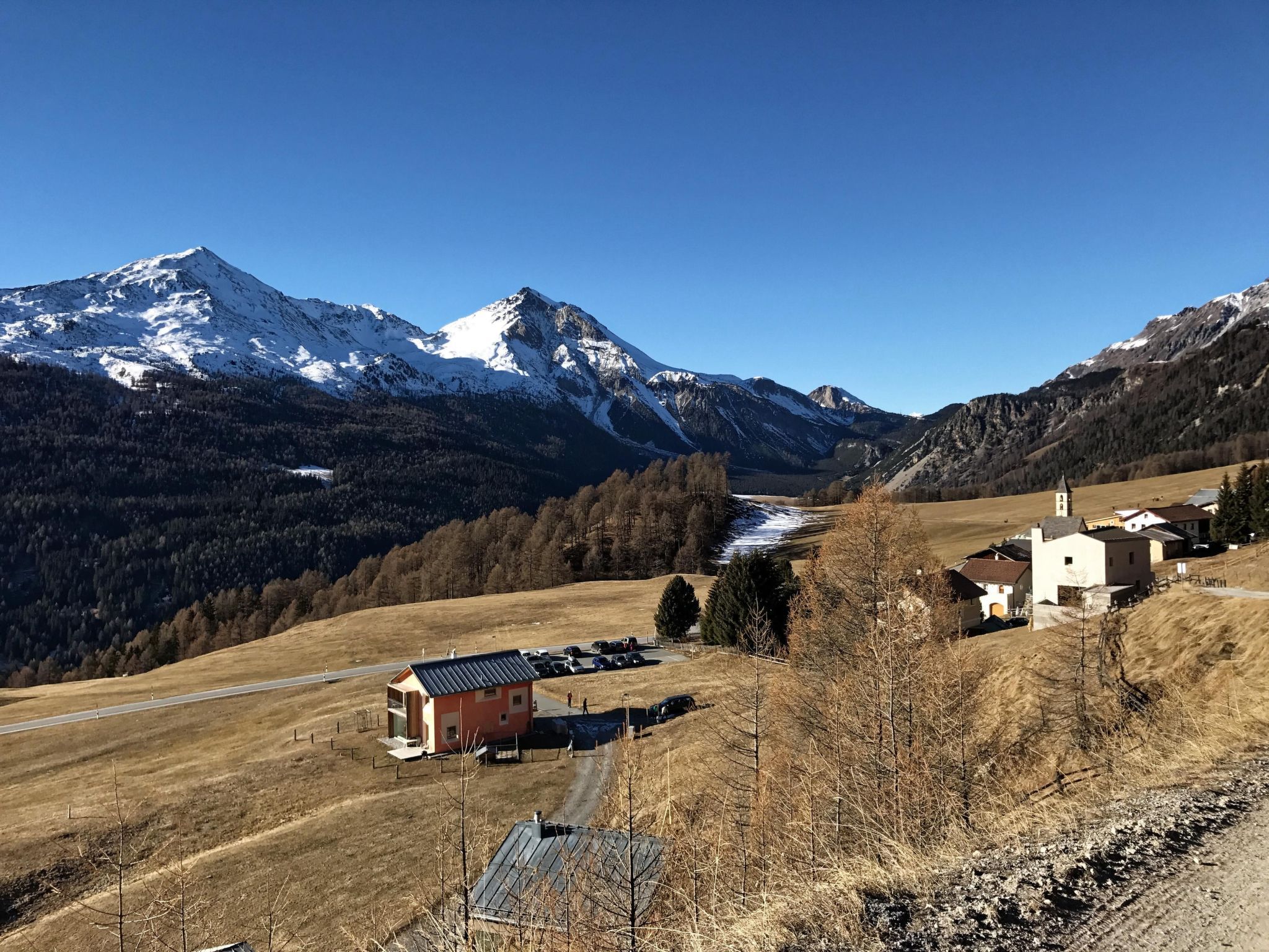 Eine Berglandschaft mit schneebedecktem Gipfel, einem kleinen Gebäude mit rotem Dach und einer Kirche mit weißer Fassade.