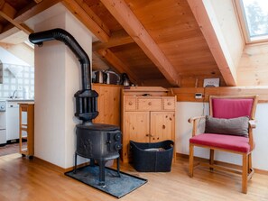 A cozy cabin interior with a wood-burning stove, wooden cabinets, a chair, and a skylight. - Ferienhaus Chasa Silva, (Lüsai) by Interhome (Lü)