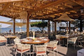An outdoor dining area with wicker furniture, tables set for meals, and a view of the sea. - Paese Serenu (Porto-Vecchio)