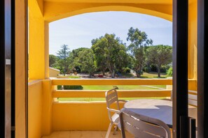 A balcony with yellow walls, a table, and a chair, overlooking a park with trees and a playground. - Paese Serenu (Porto-Vecchio)