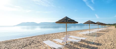A beach with white lounge chairs and thatched umbrellas.