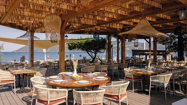An outdoor dining area with wicker furniture, tables set for meals, and a view of the sea. - Paese Serenu (Porto-Vecchio)