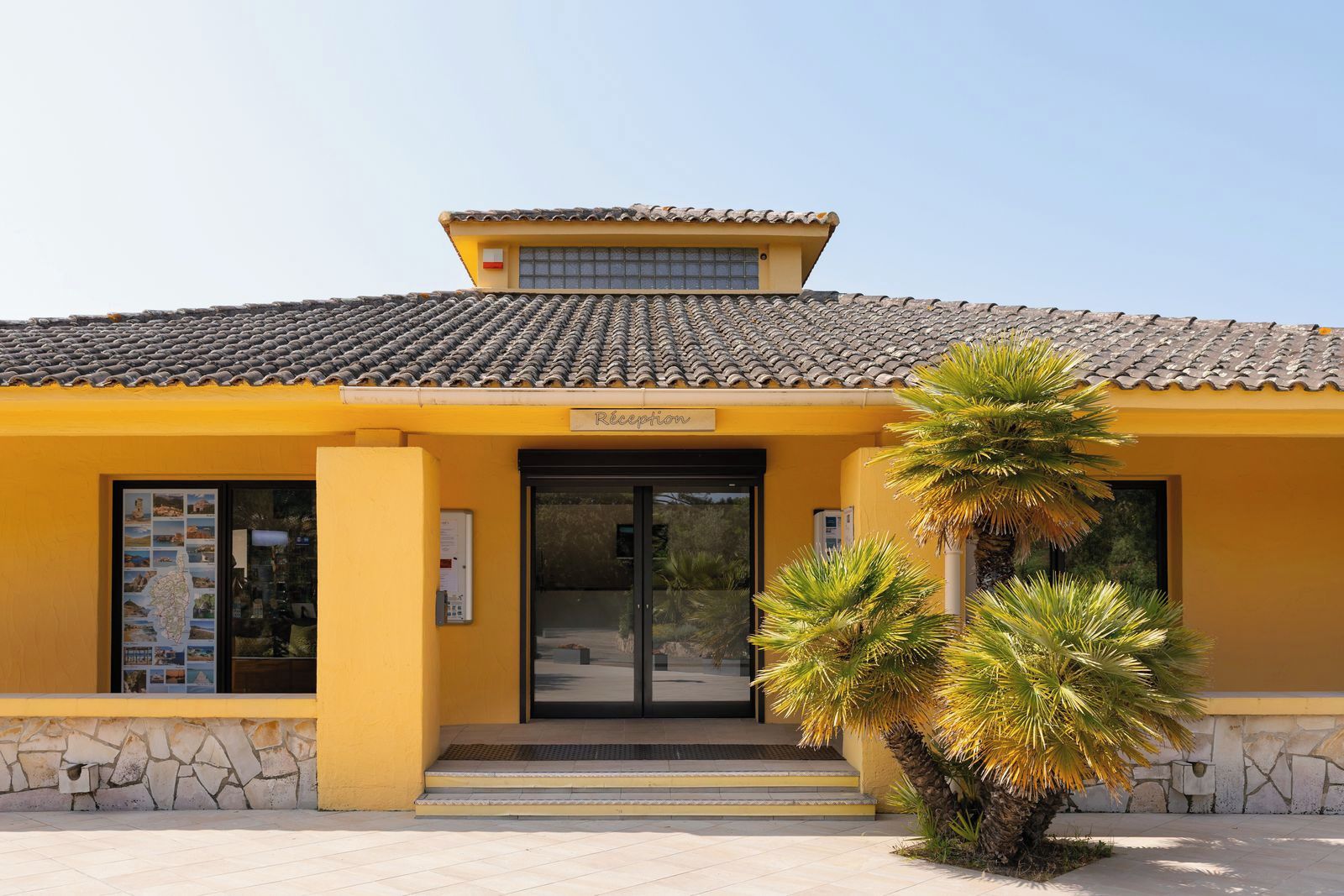 A yellow building with a tiled roof, a reception area, and a staircase leading to the entrance.