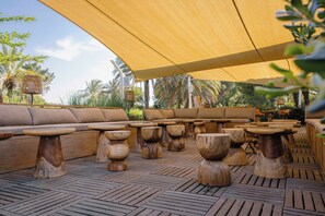 An outdoor seating area with wooden tables and sofas under a canopy. - Paese Serenu (Porto-Vecchio)