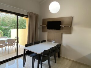 A room with a large sliding glass door leading to an outdoor area, a flat-screen TV mounted on the wall, a white table with chairs, and a ceiling light fixture. - Paese Serenu (Porto-Vecchio)
