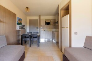 A compact room with a bed, a dining table with chairs, a kitchenette with a refrigerator, and a small seating area. - Paese Serenu (Porto-Vecchio)