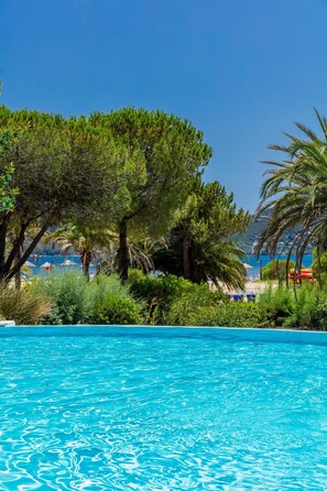 Una piscina azul cristalina rodeada de abundante follaje y palmeras, con vista al mar.
