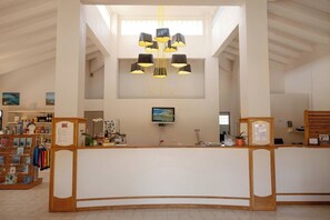 A reception area with a curved desk, a television mounted on the wall, and a chandelier with multiple lamps. - Paese Serenu (Porto-Vecchio)