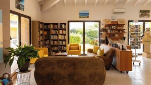 A spacious living room with a large bookshelf, a comfortable sofa, a coffee table, and a view of the outdoors. - Paese Serenu (Porto-Vecchio)