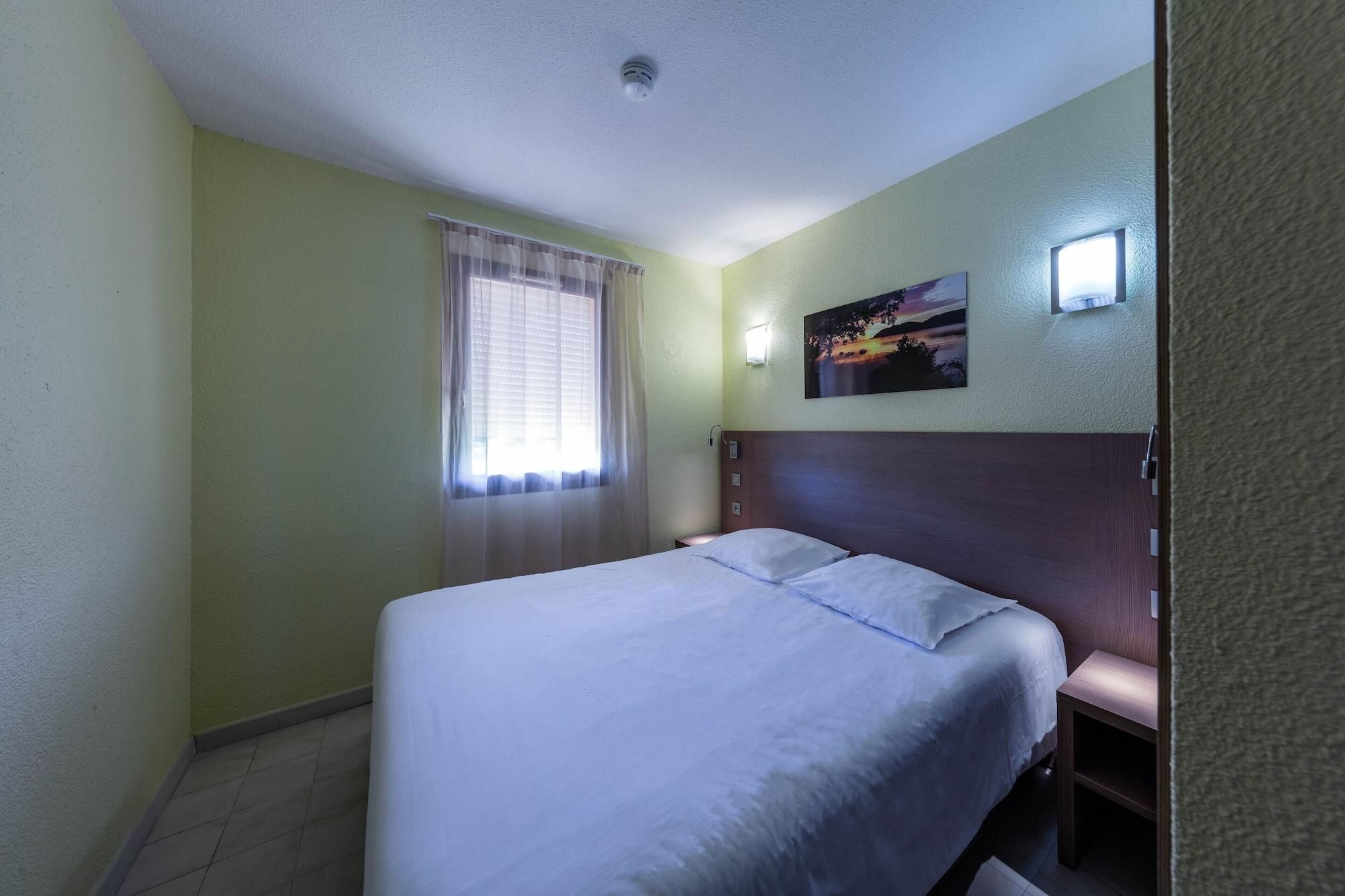 A hotel room with a bed, a window with curtains, a wall-mounted picture, and a ceiling light.