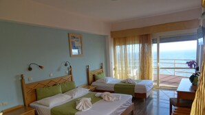 Habitación de hotel con dos camas, cabecera de madera, una mesita y vistas al mar a través de amplias ventanas.