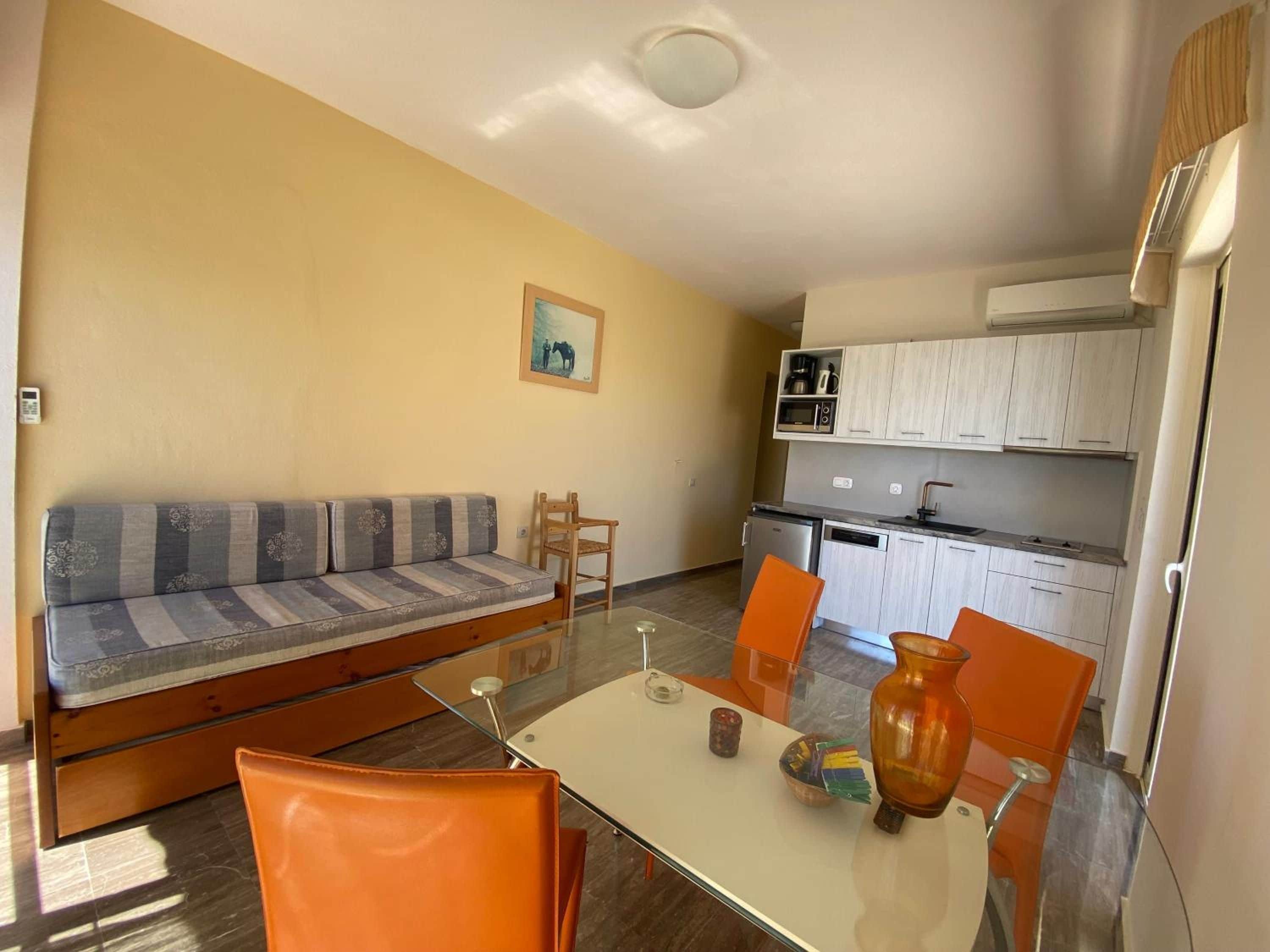 Un espacio habitable compacto con sofá, mesa de comedor, sillas, área de cocina y una pequeña mesa con un florero.