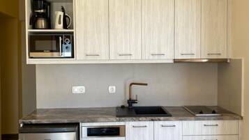 Una cocina compacta con lavavajillas integrado, cafetera, microondas y estufa a gas.