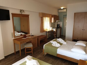 Une chambre d’hôtel comprenant un lit, un bureau avec une chaise, un miroir, une petite kitchenette et une armoire.