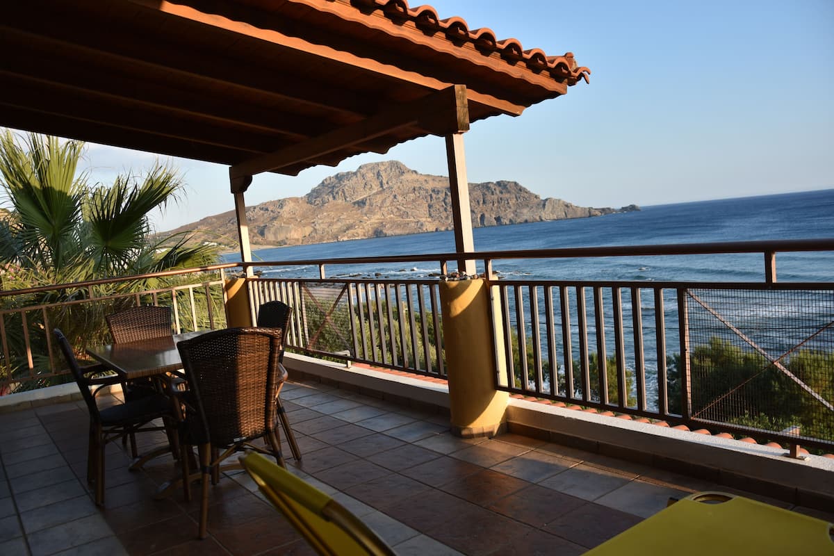 A covered outdoor seating area with a view of the sea and mountains.