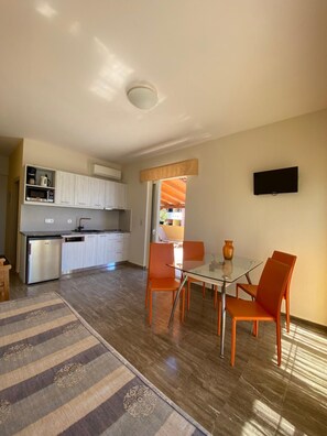 Un espace de vie compact comprenant un coin cuisine, un coin repas et un téléviseur fixé au mur.