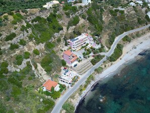 Vue aérienne d’une propriété située sur la côte, comprenant plusieurs bâtiments, une route et une plage.