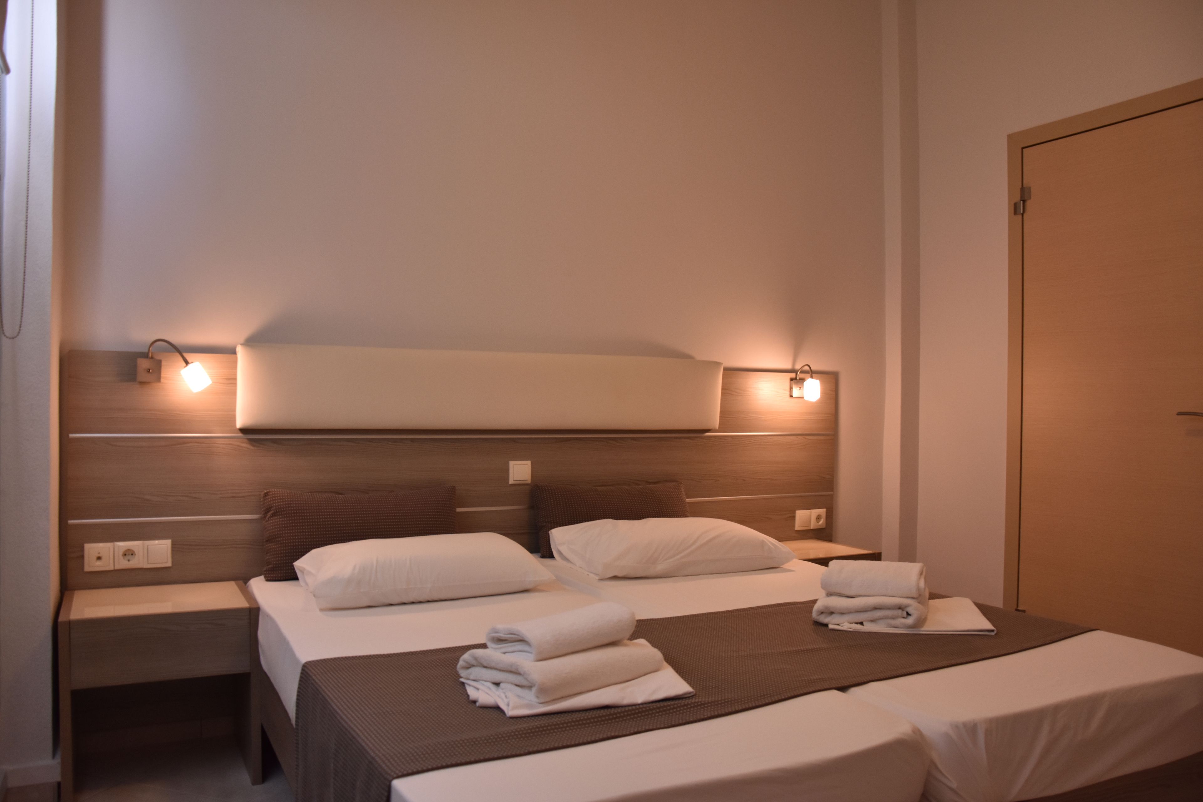 Habitación de hotel con dos camas, cabecero de madera, lámparas de noche y una puerta.